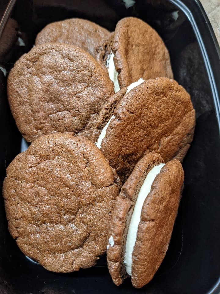 Homemade chocolate sandwich cookies with cream filling in a black container