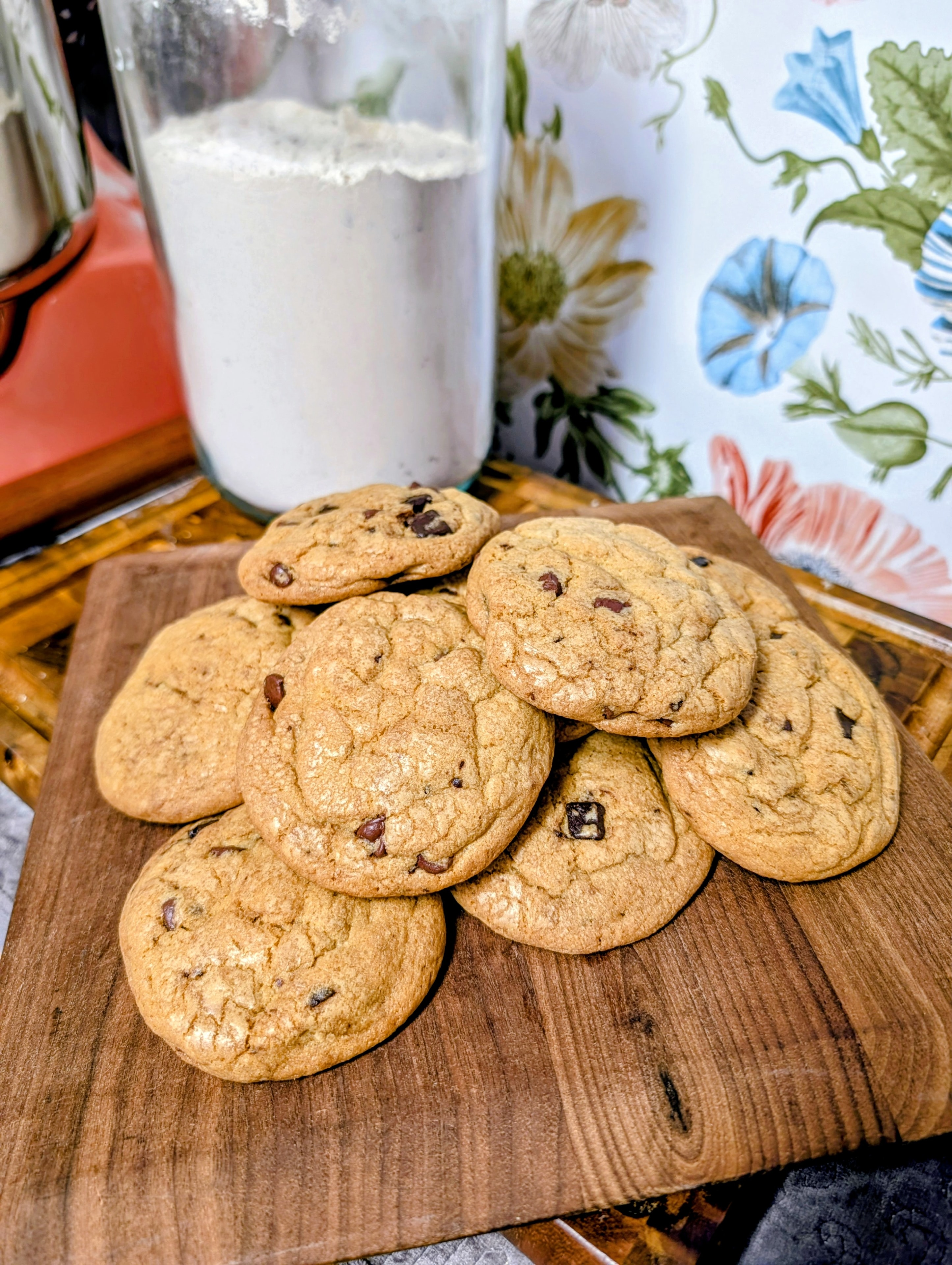 Chocolate chip cookies piled on a wooden board with a glass of milk