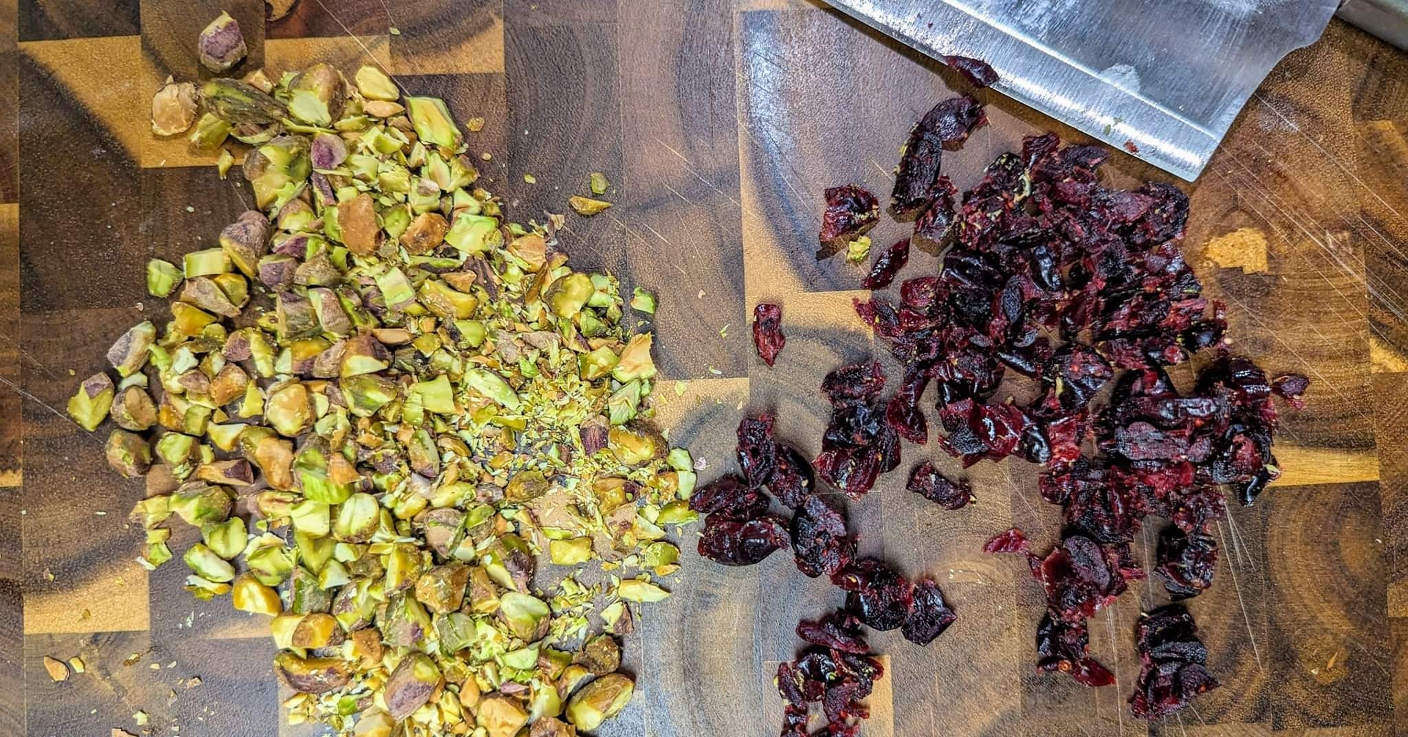 Chopped pistachios and dried cranberries on a wood cutting board