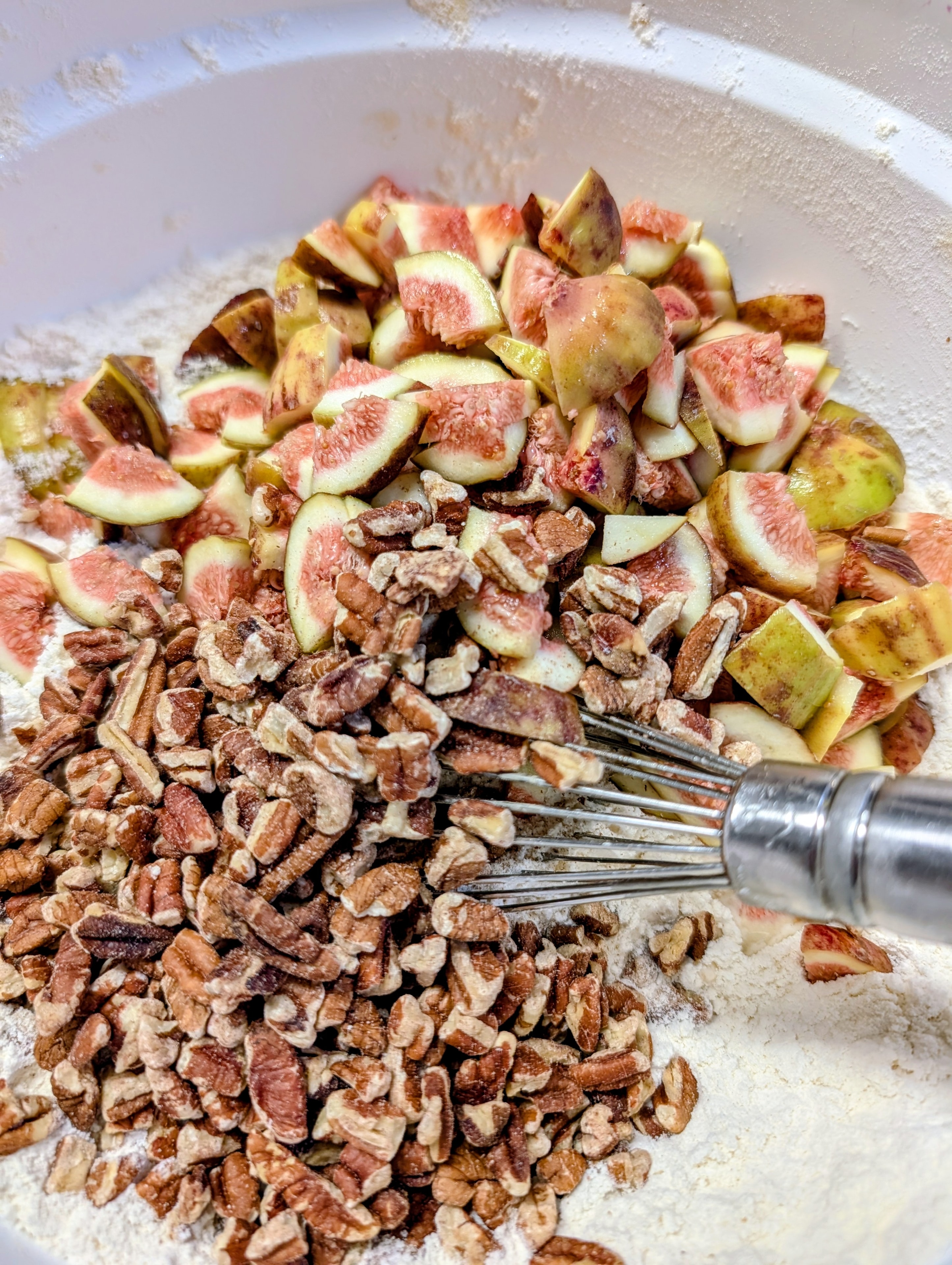 Fresh figs and chopped walnuts in a mixing bowl with flour and a whisk