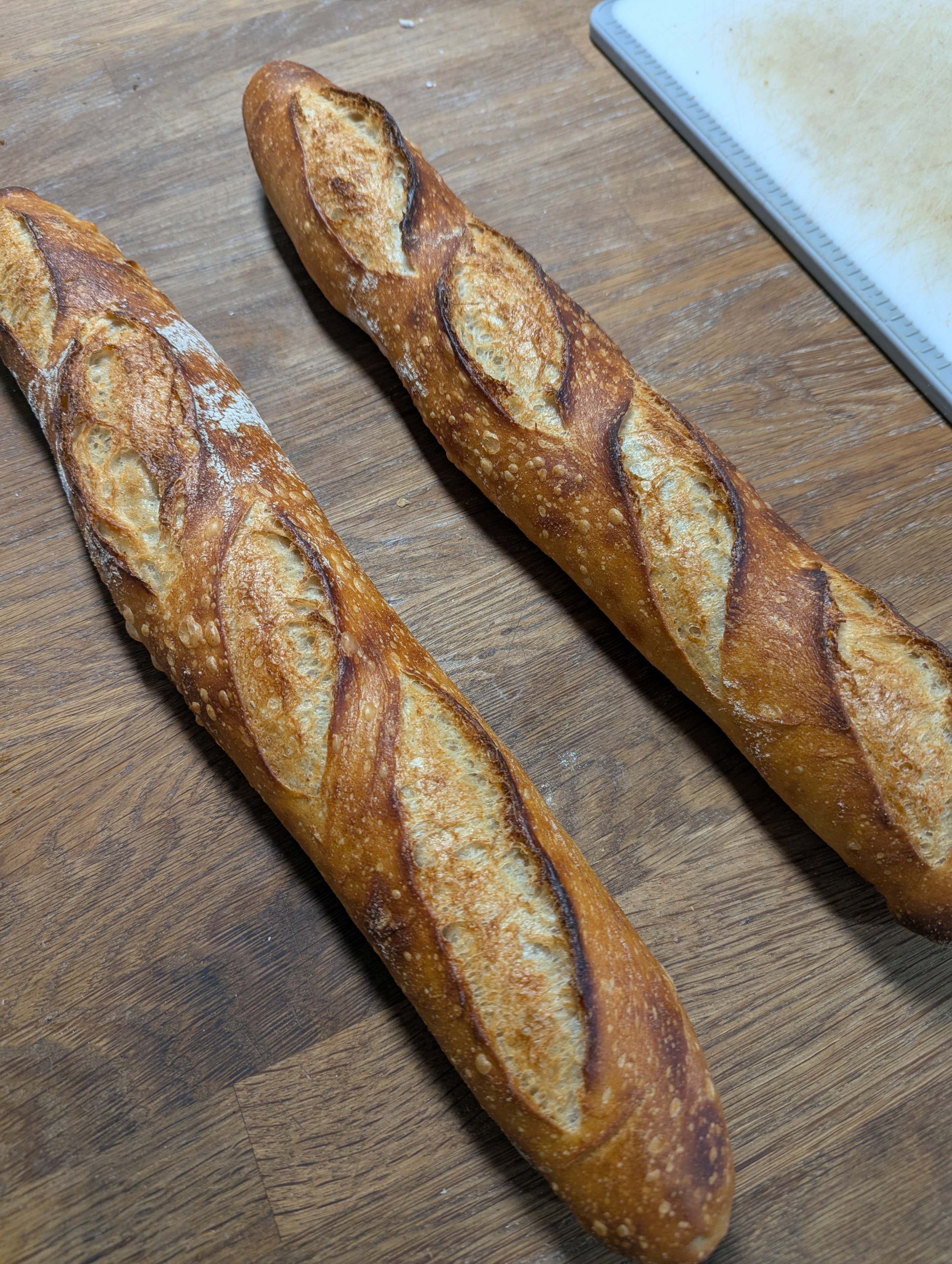 Two golden sourdough baguettes on a wooden surface