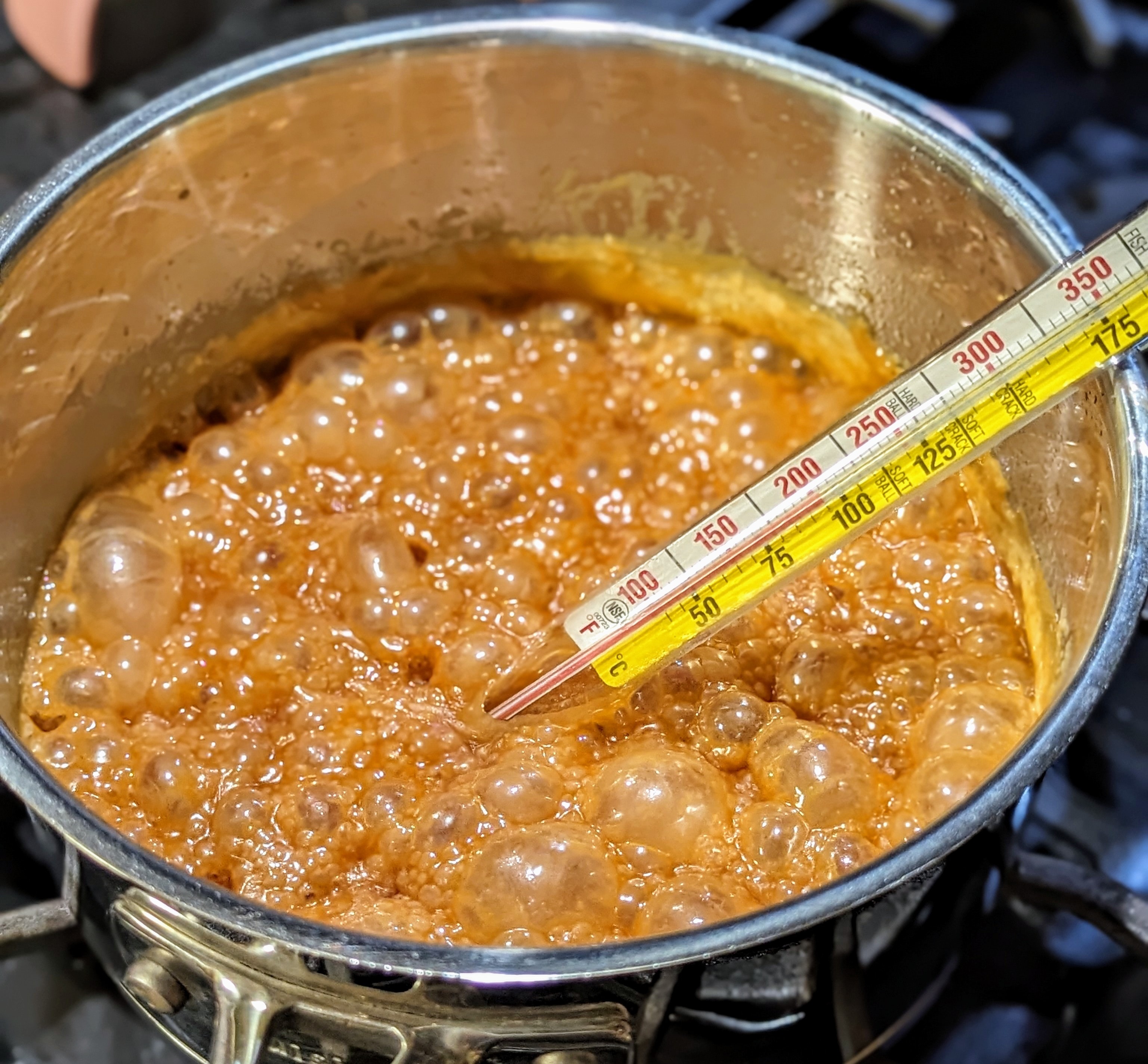 Bubbling caramel mixture in a pot with a candy thermometer